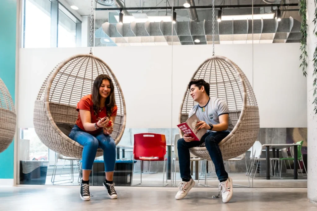 Two students sitting in chairs studying a textbook together on campus